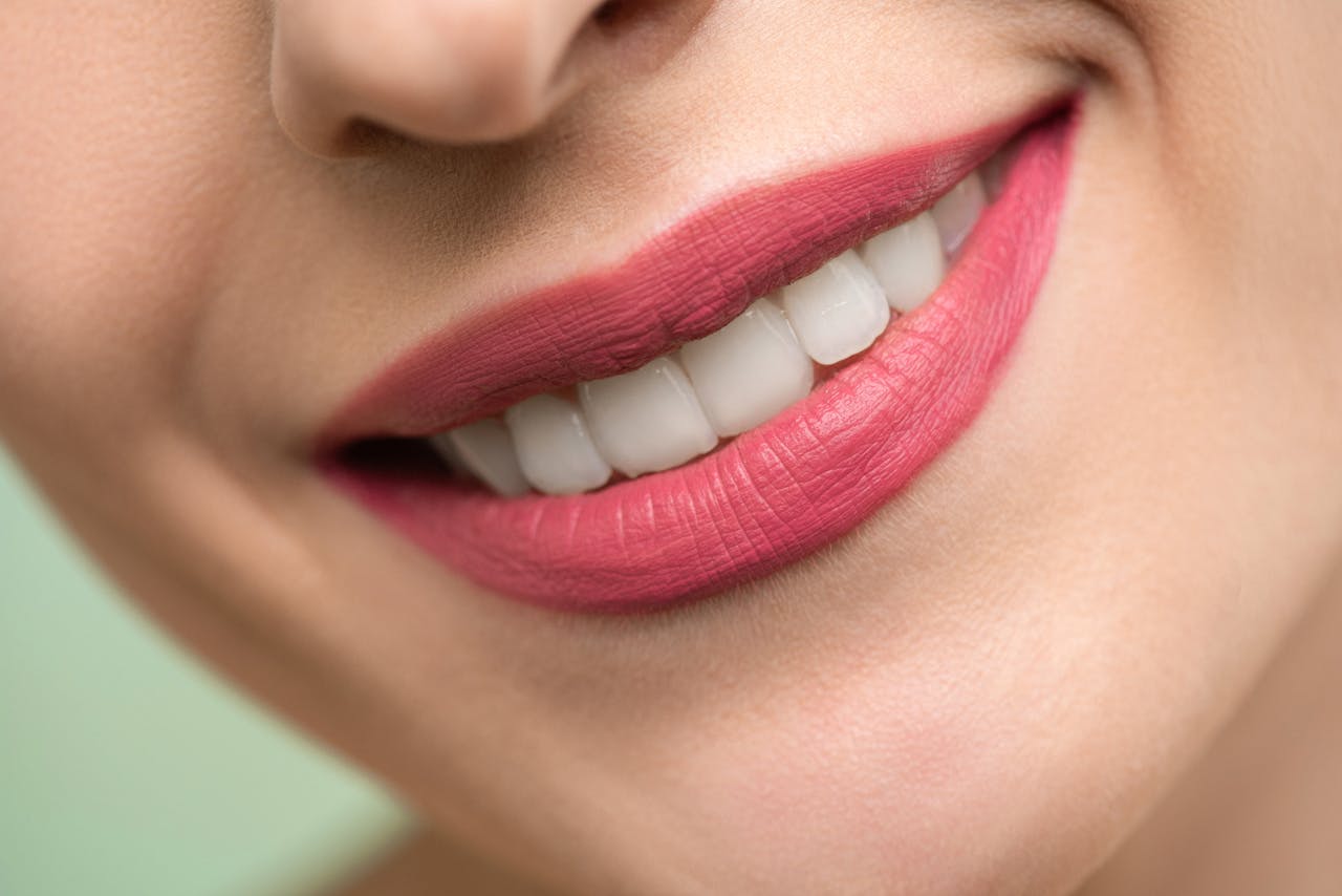 Vivid close-up image of a womans smile showcasing red lipstick and white teeth on a light background.